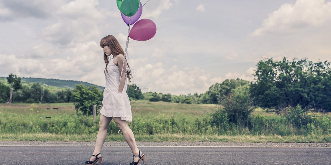 Kobieta w sukience i szpilkach idąca drogą z balonami w dłoni, pokazująca wysmuklającą stylizację.