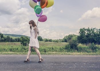 Kobieta w sukience i szpilkach idąca drogą z balonami w dłoni, pokazująca wysmuklającą stylizację.
