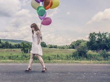 Kobieta w sukience i szpilkach idąca drogą z balonami w dłoni, pokazująca wysmuklającą stylizację.