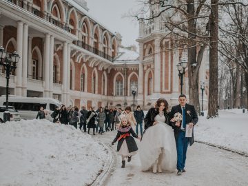 Para młoda i goście weselni idą zimową, ośnieżoną alejką przy zabytkowym pałacu