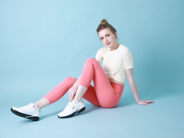 Kobieta w stroju sportowym siedzi w białych butach i różowych legginsach